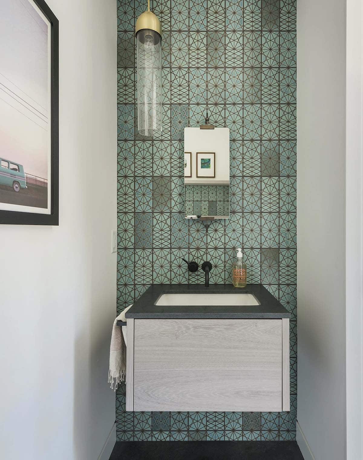 Powder room with intricate teal geometric tile, floating wood vanity, and hanging glass pendant light