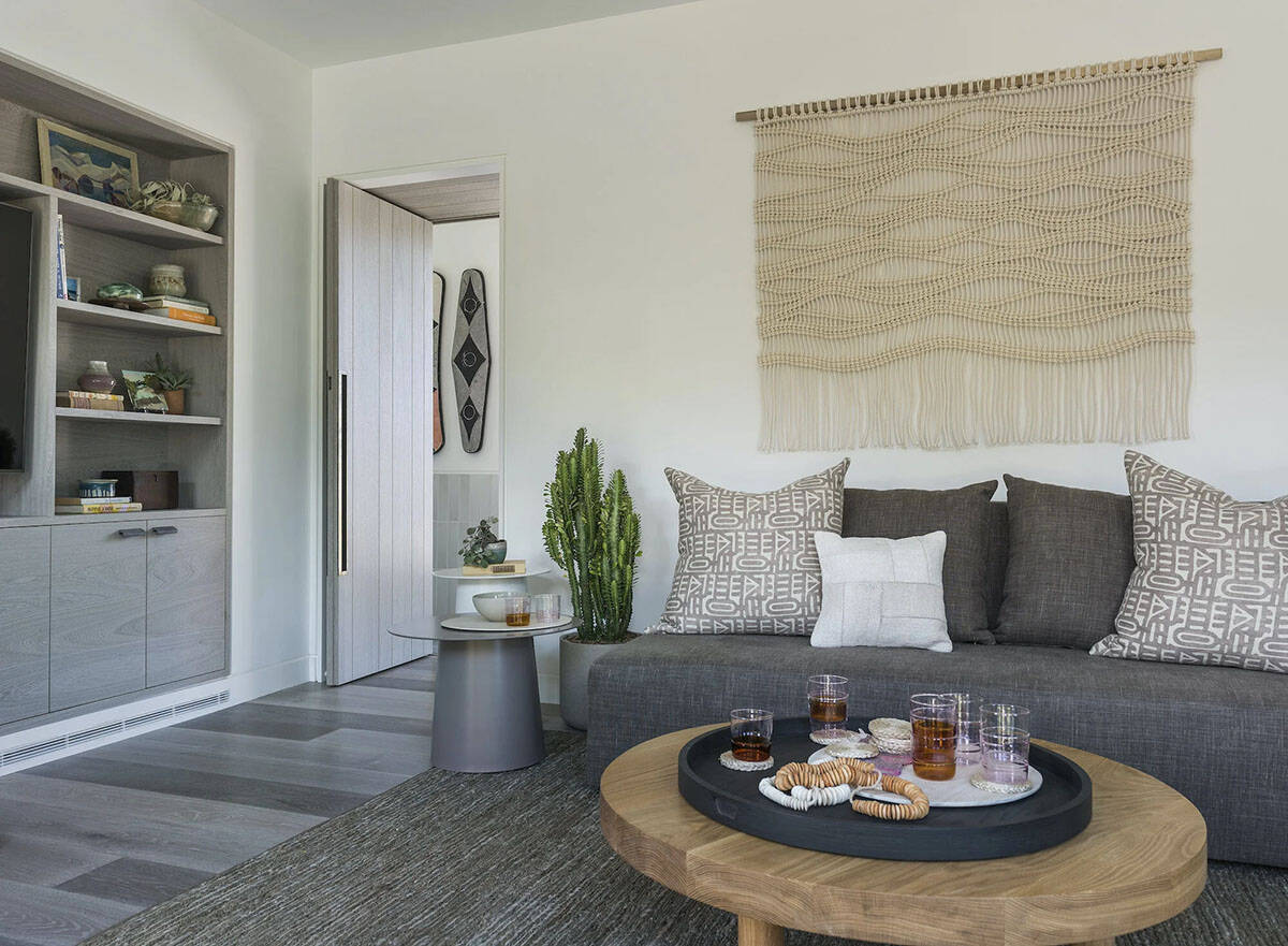 Living room corner with gray sofa, patterned pillows, macrame wall hanging, and round wood coffee table