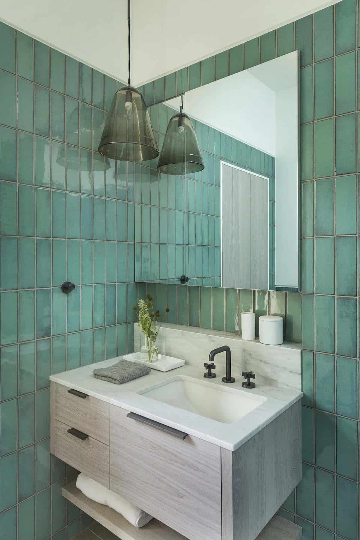 Bathroom vanity with glossy green vertical tile, marble countertop, black fixtures, and pendant lighting