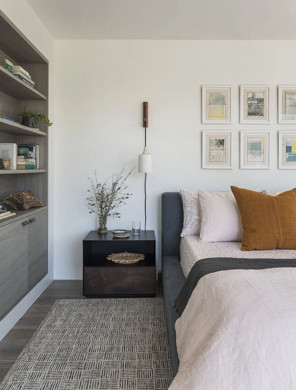 Bedroom nightstand detail with black cabinet, pendant wall lamp, framed gallery art, and a gray upholstered daybed
