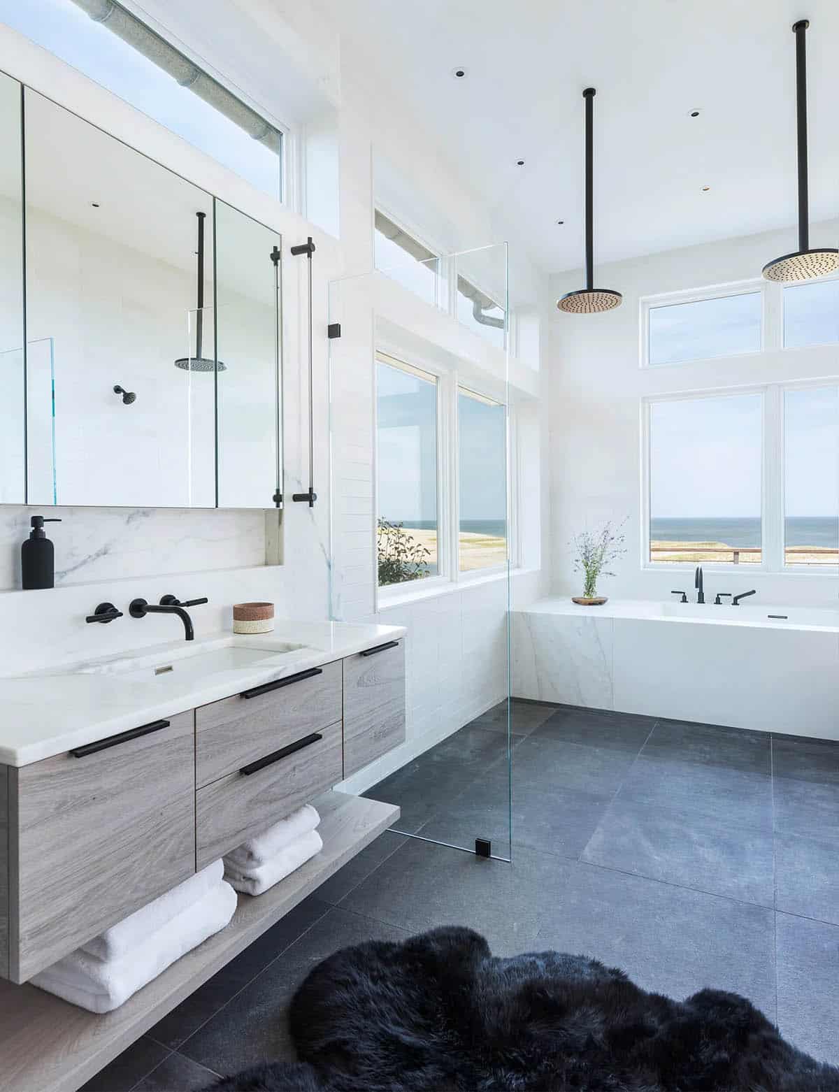 Primary bathroom with floating wood vanity, soaking tub, glass shower divider, and ocean-view windows