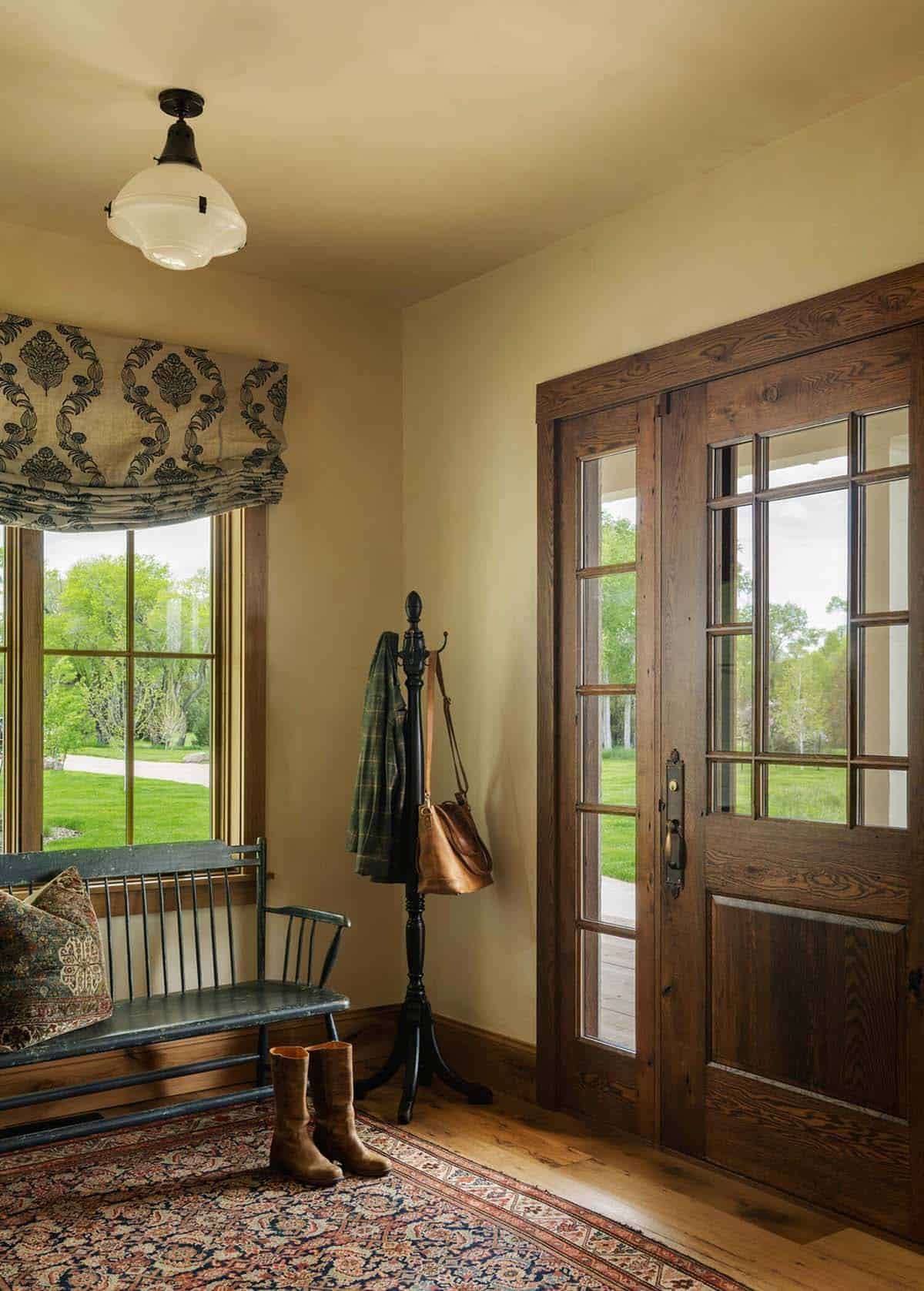 Rustic entryway with wood-paned front door, antique bench, coat rack, and leather boots on patterned rug