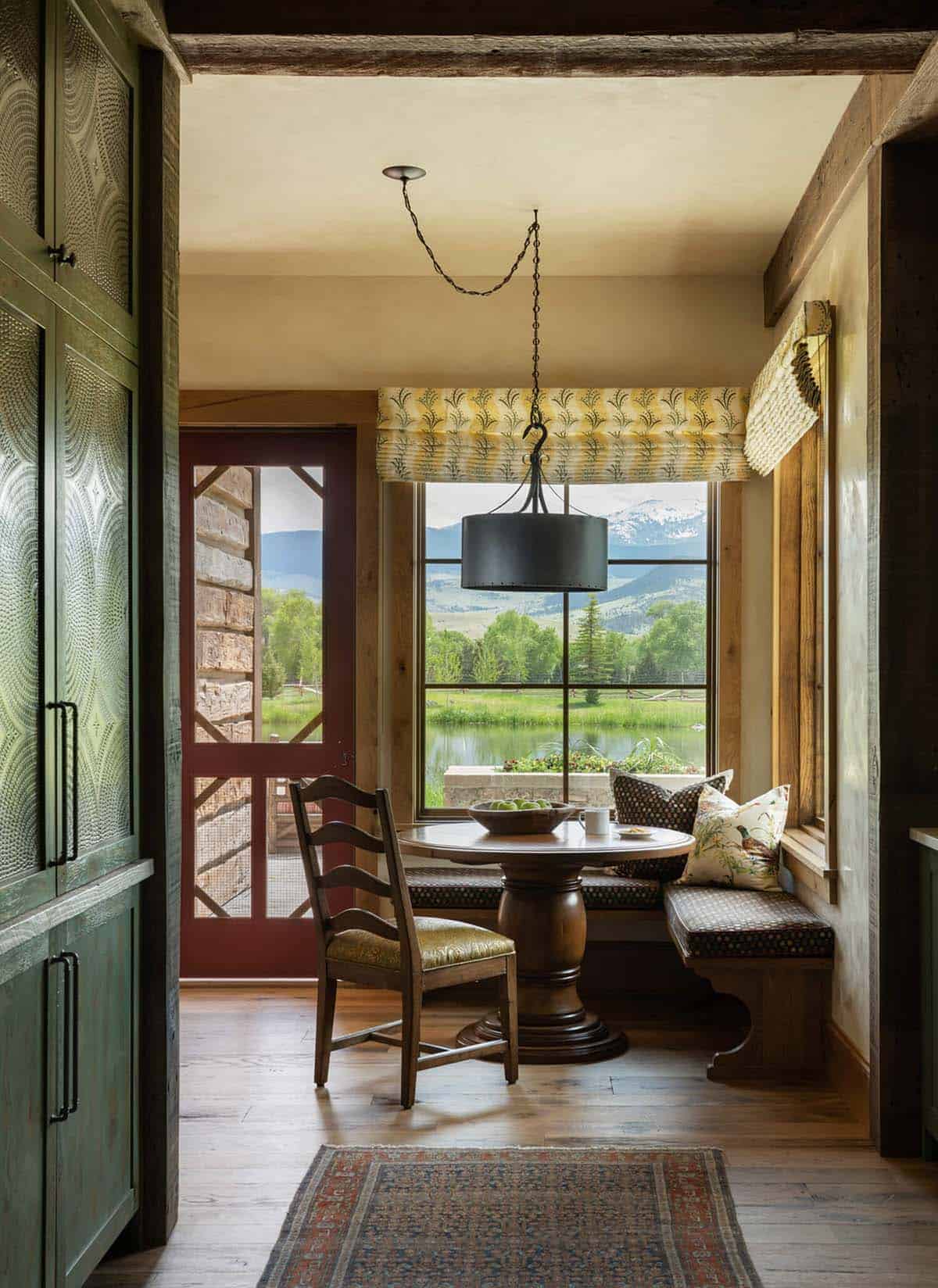 Breakfast nook with round wood table, banquette seating, and large window overlooking a pond and mountains