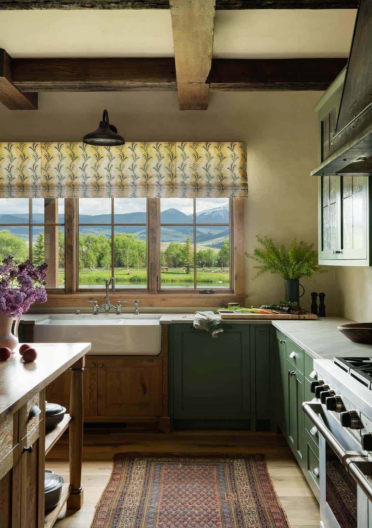 Kitchen sink area with farmhouse sink, green cabinets, and large window framing mountain and pasture views