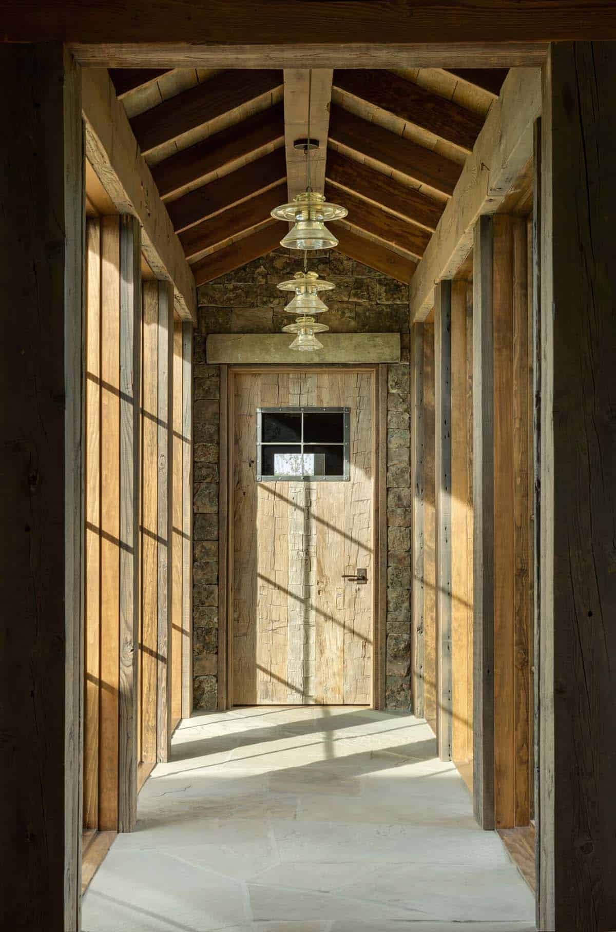 Narrow wood-paneled hallway leading to a rustic plank door under glass pendant lights