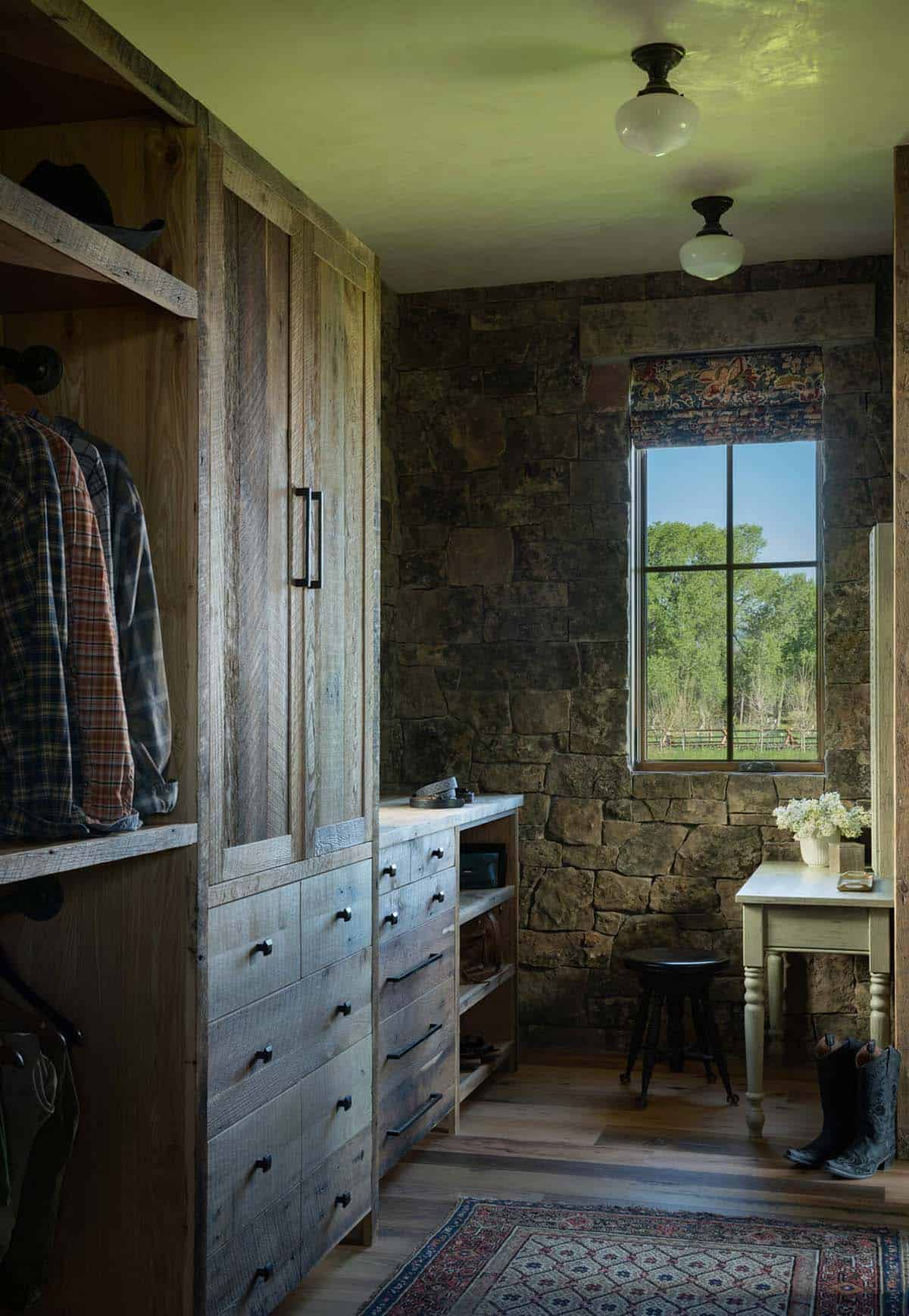 Rustic dressing room with reclaimed wood built-in drawers, stone wall, vanity table, and cowboy boots