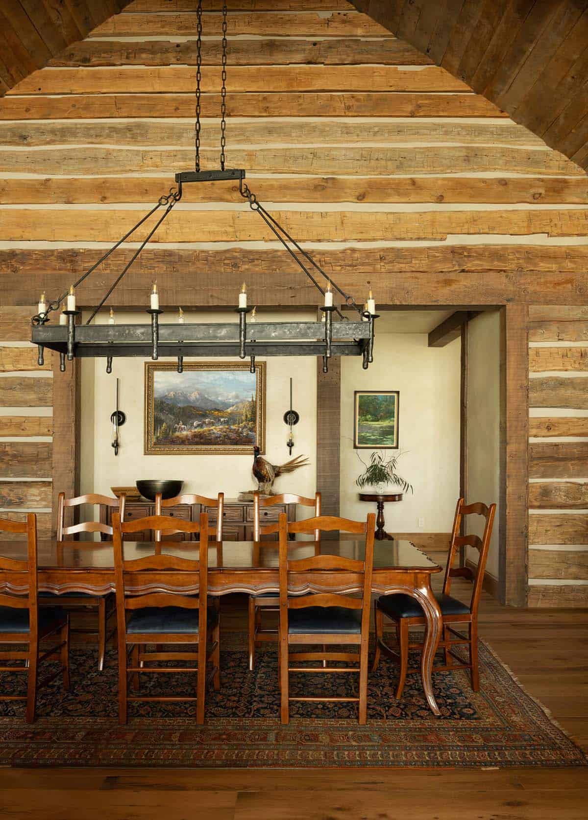 Log cabin dining room with wrought-iron candle chandelier over a wood table and leather-seated chairs