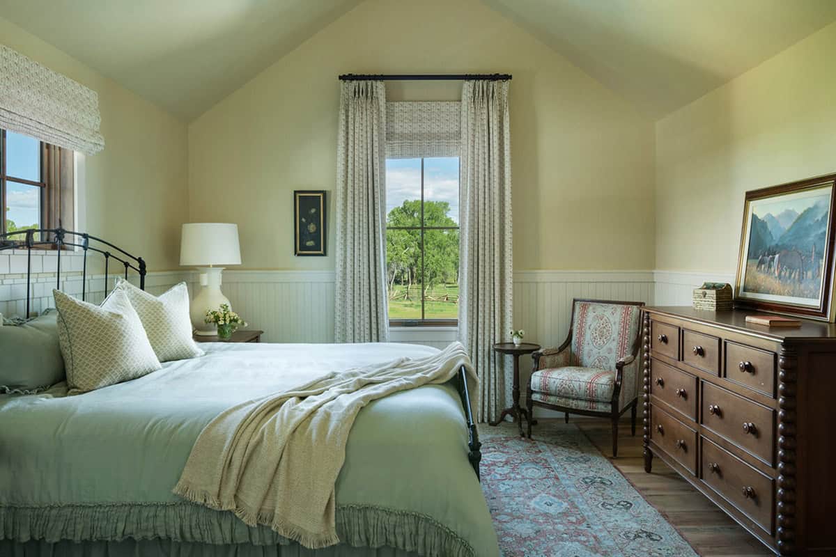 Guest bedroom with iron bed frame, green bedding, wainscoting, and a window overlooking pastureland
