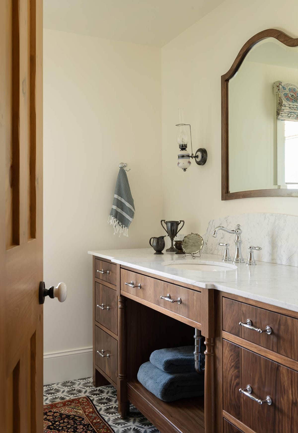 Bathroom vanity with marble countertop, wood cabinetry, arched mirror, and vintage silver accessories