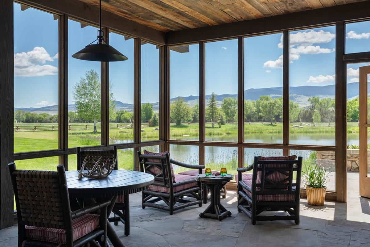 Screened porch with wicker chairs and round table overlooking a pond and mountain pasture views