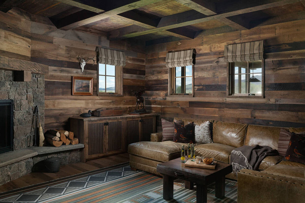 Reclaimed wood-clad den with leather sectional, striped rug, and stone fireplace stocked with firewood