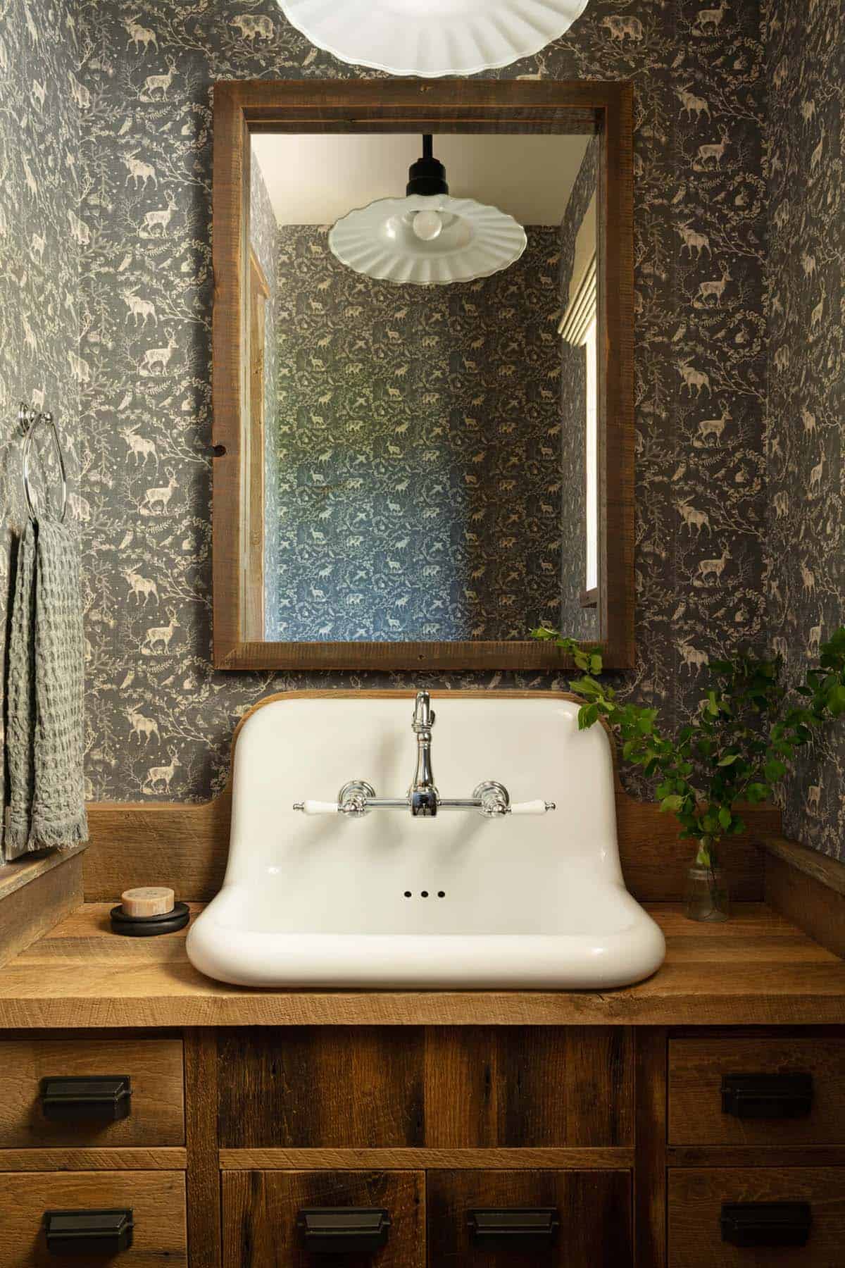 Powder room with woodland-print wallpaper, farmhouse sink, wood-framed mirror, and schoolhouse light fixture