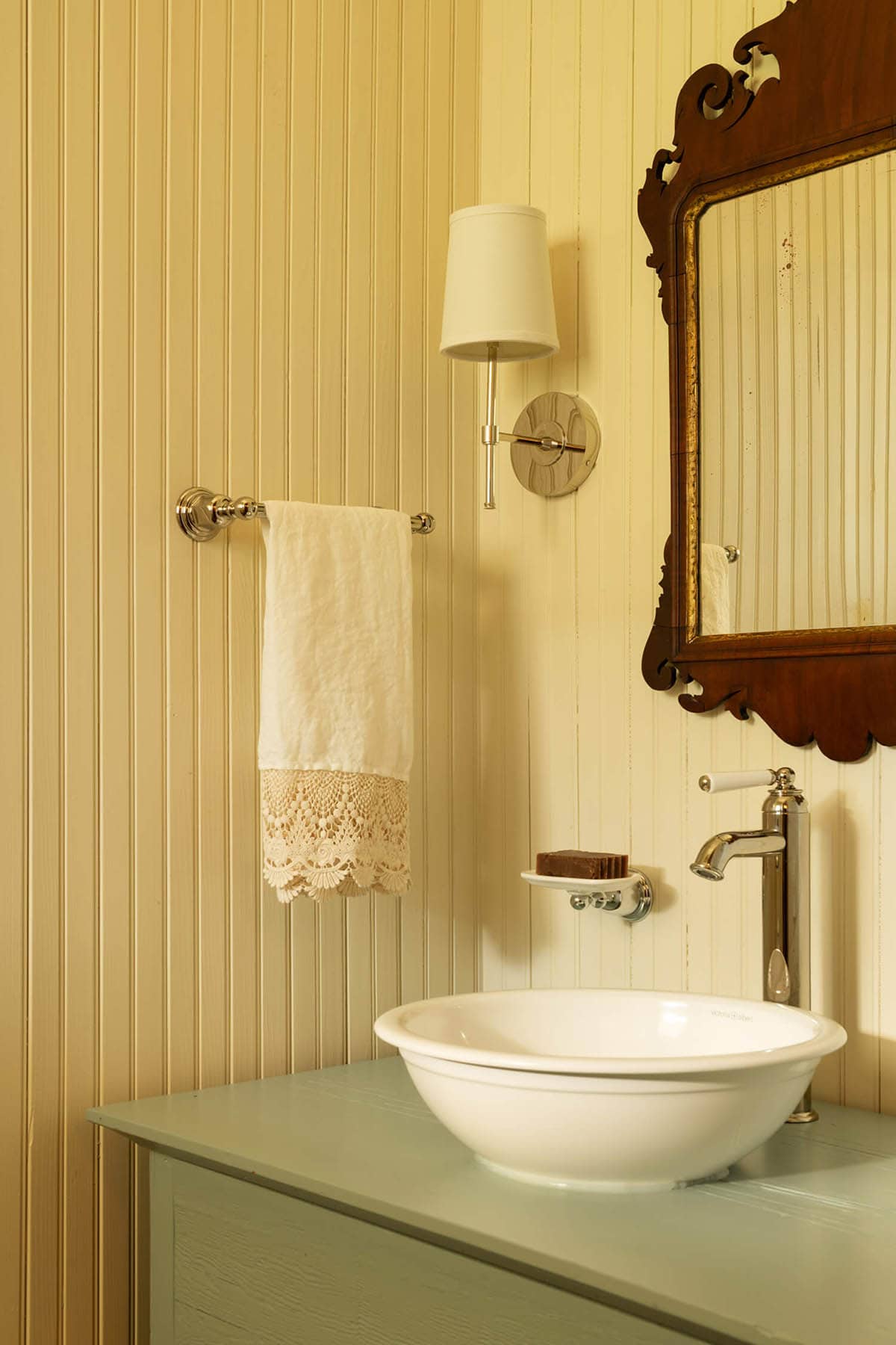 Vintage-style bathroom vignette with vessel sink, ornate mirror, sconce, and lace-trimmed hand towel