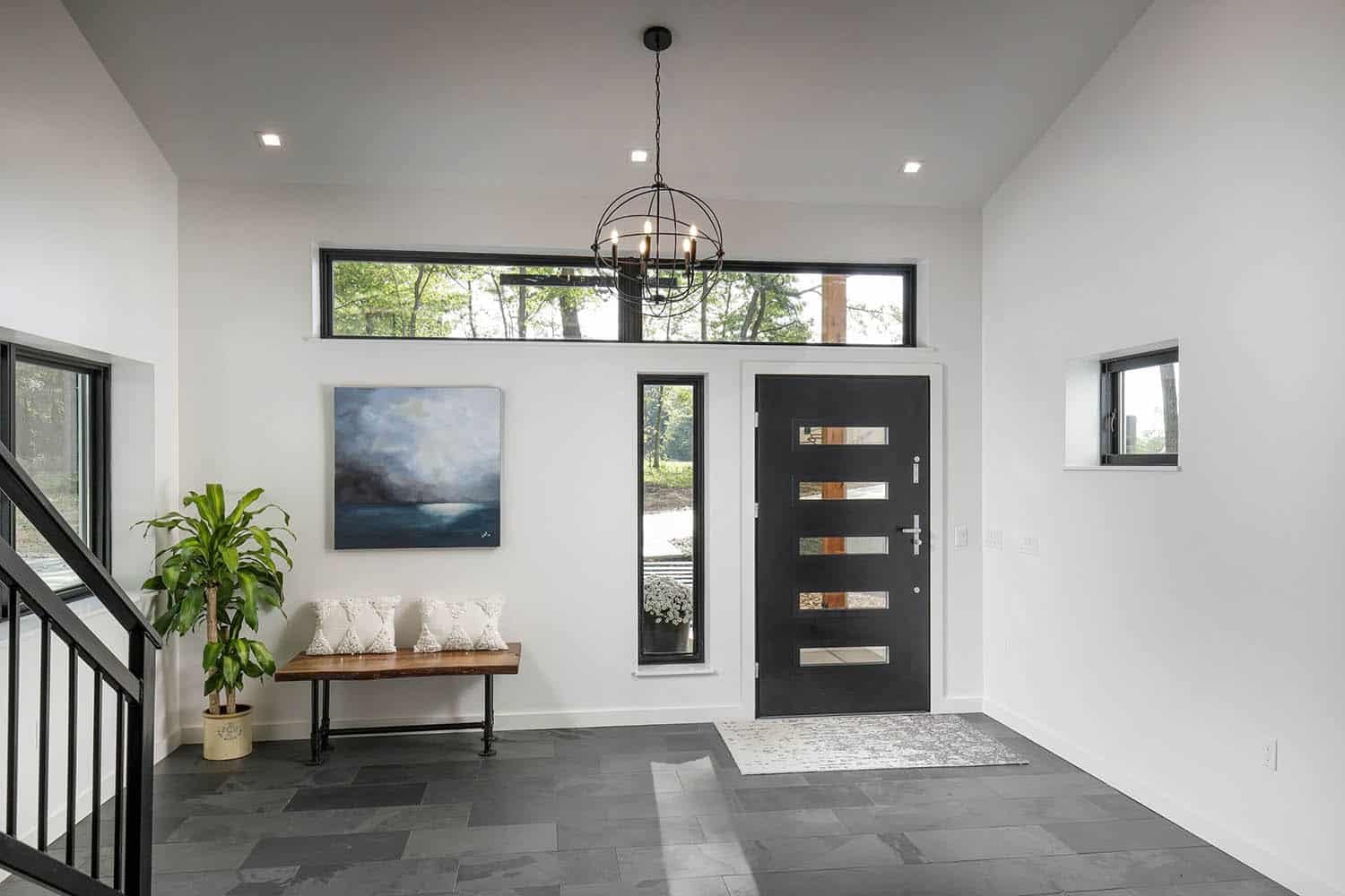 Entryway with slate tile floor, black front door with glass inserts, wood bench, potted plant, and orb chandelier