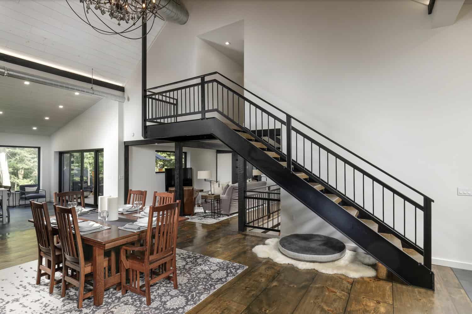 Dining area with wood table and chairs beneath a black open staircase with steel railings and a round dog bed underneath