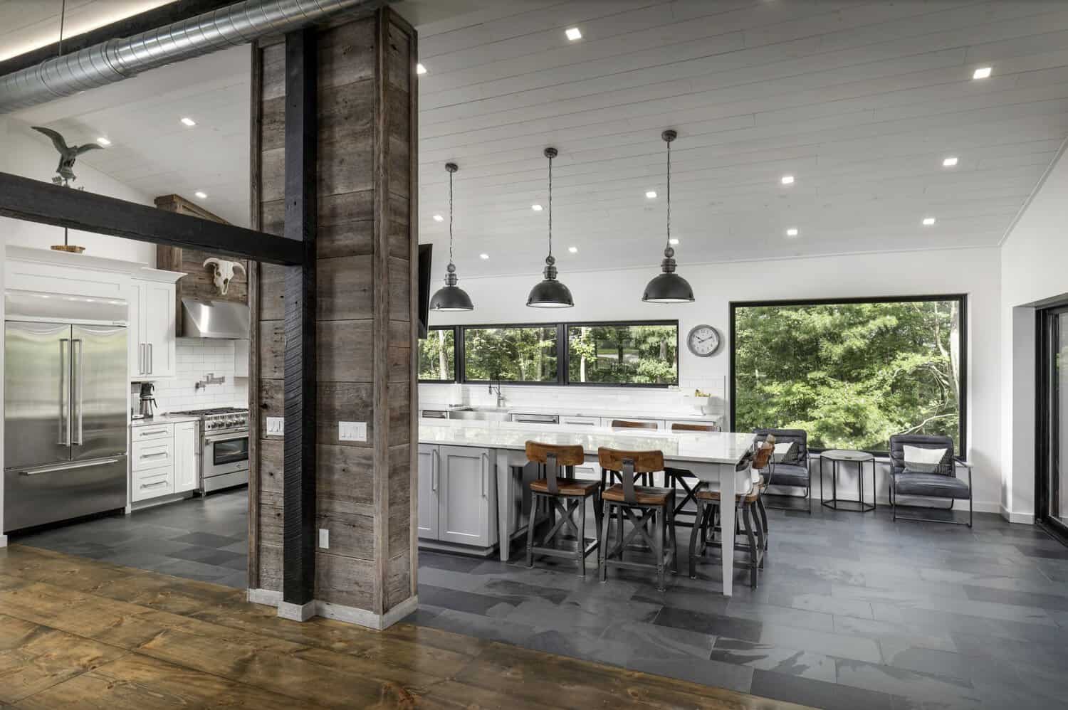 Kitchen with reclaimed wood support column, stainless fridge, subway tile backsplash, and dining table by large forest-view window