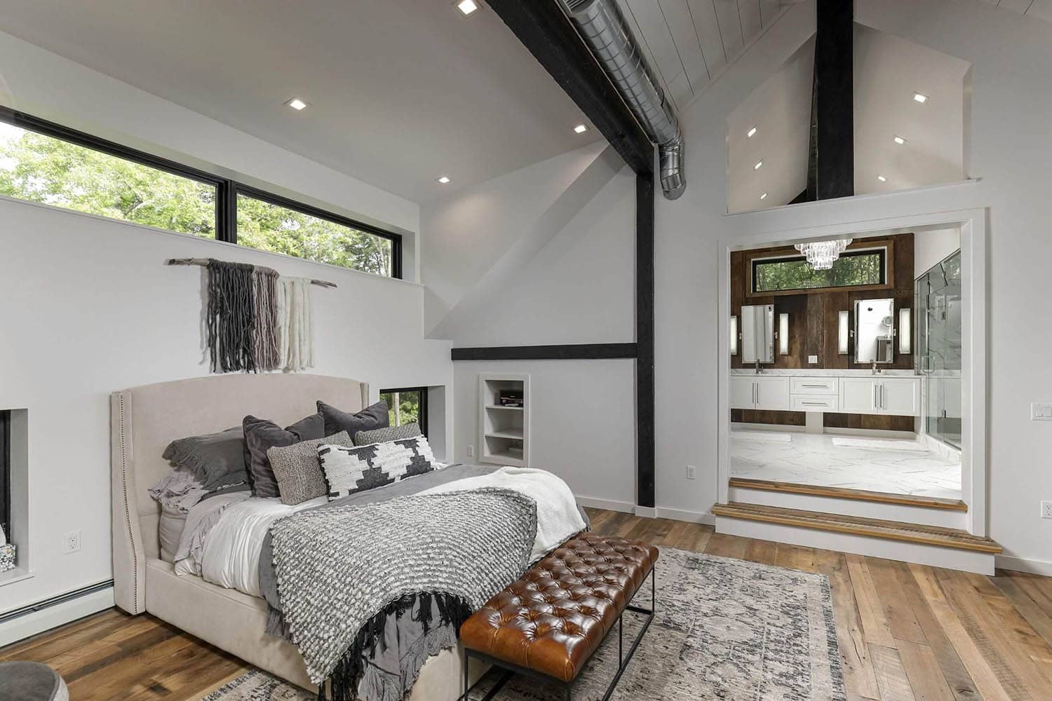 Bedroom with vaulted shiplap ceiling, black exposed beam, large ceiling fan, TV console, and leather bench at foot of bed