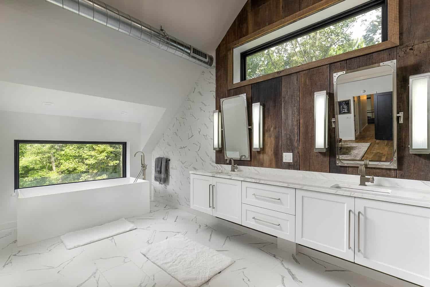 Primary bathroom with floating white double vanity, reclaimed wood accent wall, mirrors, and freestanding tub by window