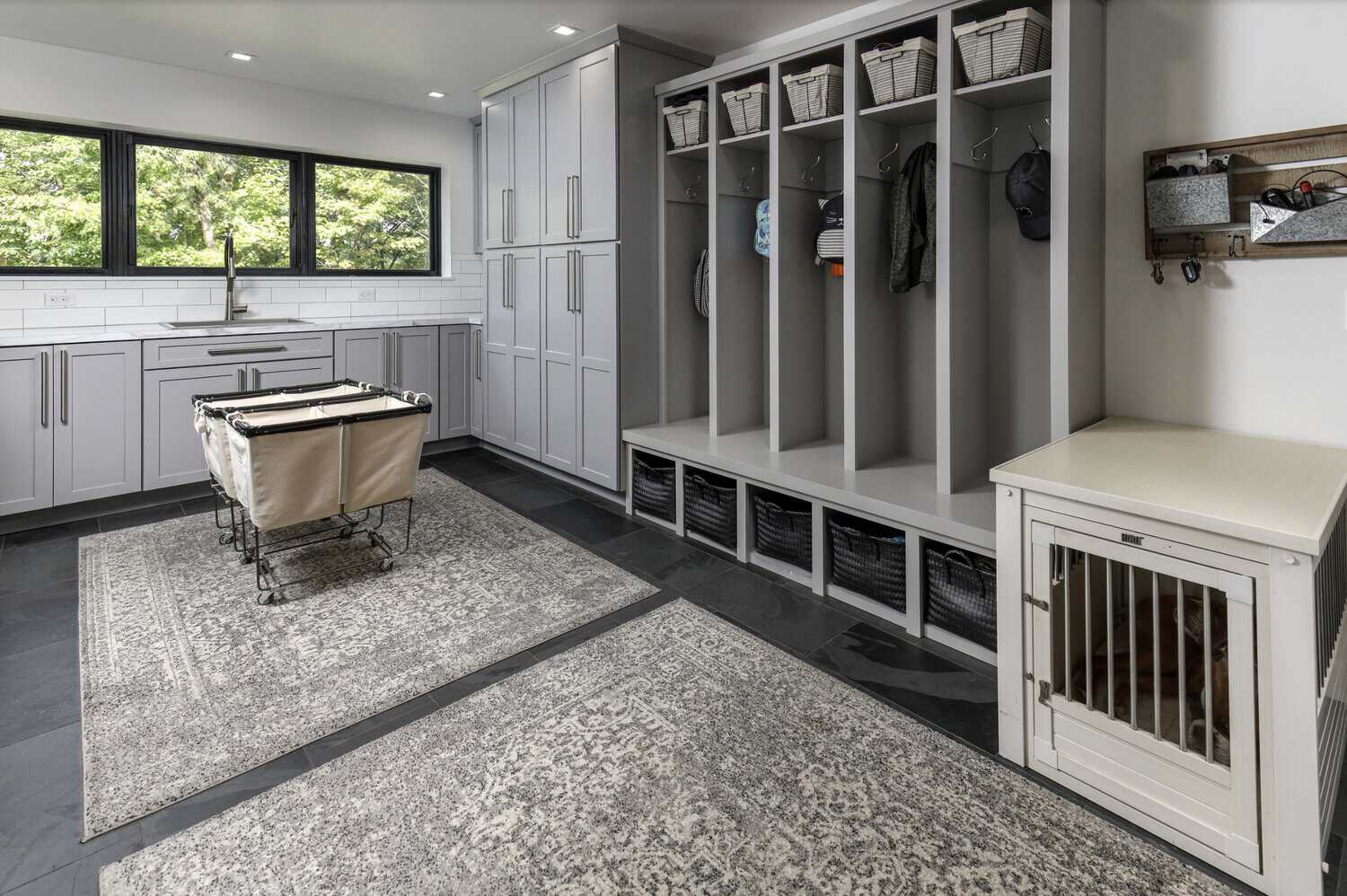 Mudroom/laundry room with gray built-in lockers, woven baskets, rolling laundry cart, and built-in dog crate