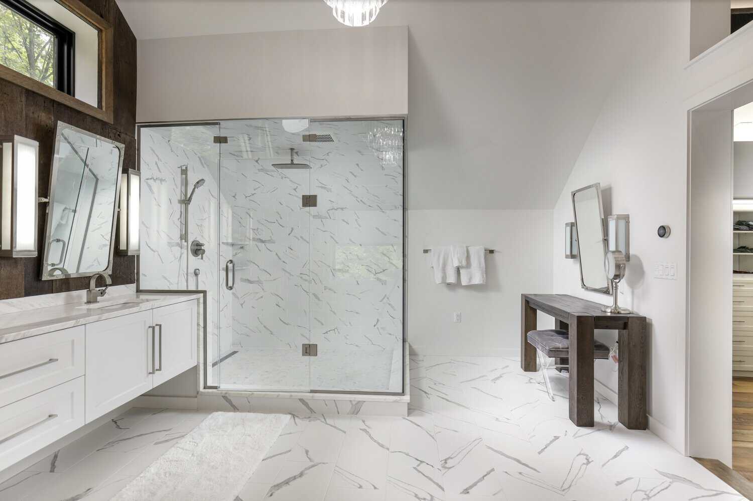 Bathroom with glass-enclosed marble shower, floating white vanity, wood accent wall, and dark wood vanity desk