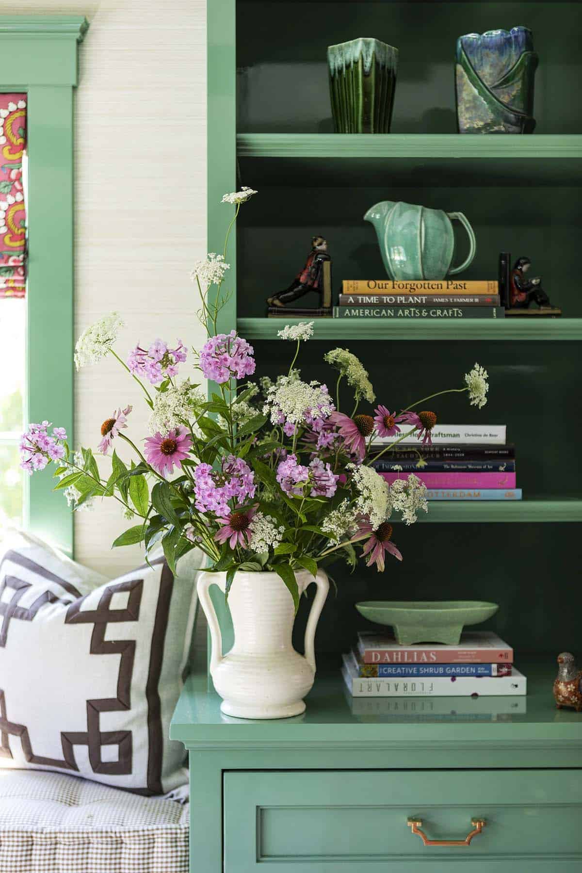 Green built-in shelving with wildflower bouquet in white pitcher and decorative books and pottery