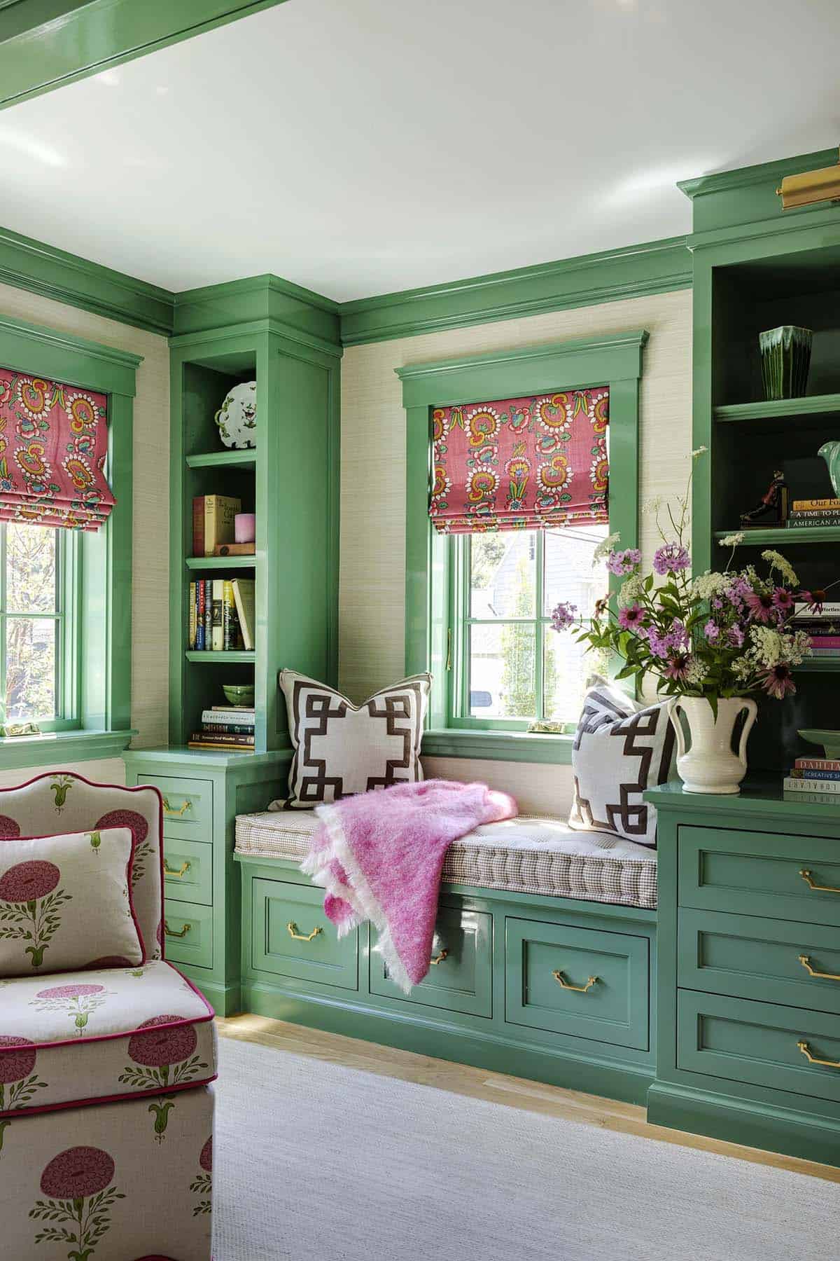 Green built-in window seat with striped cushion, graphic pillows, and a pink throw blanket