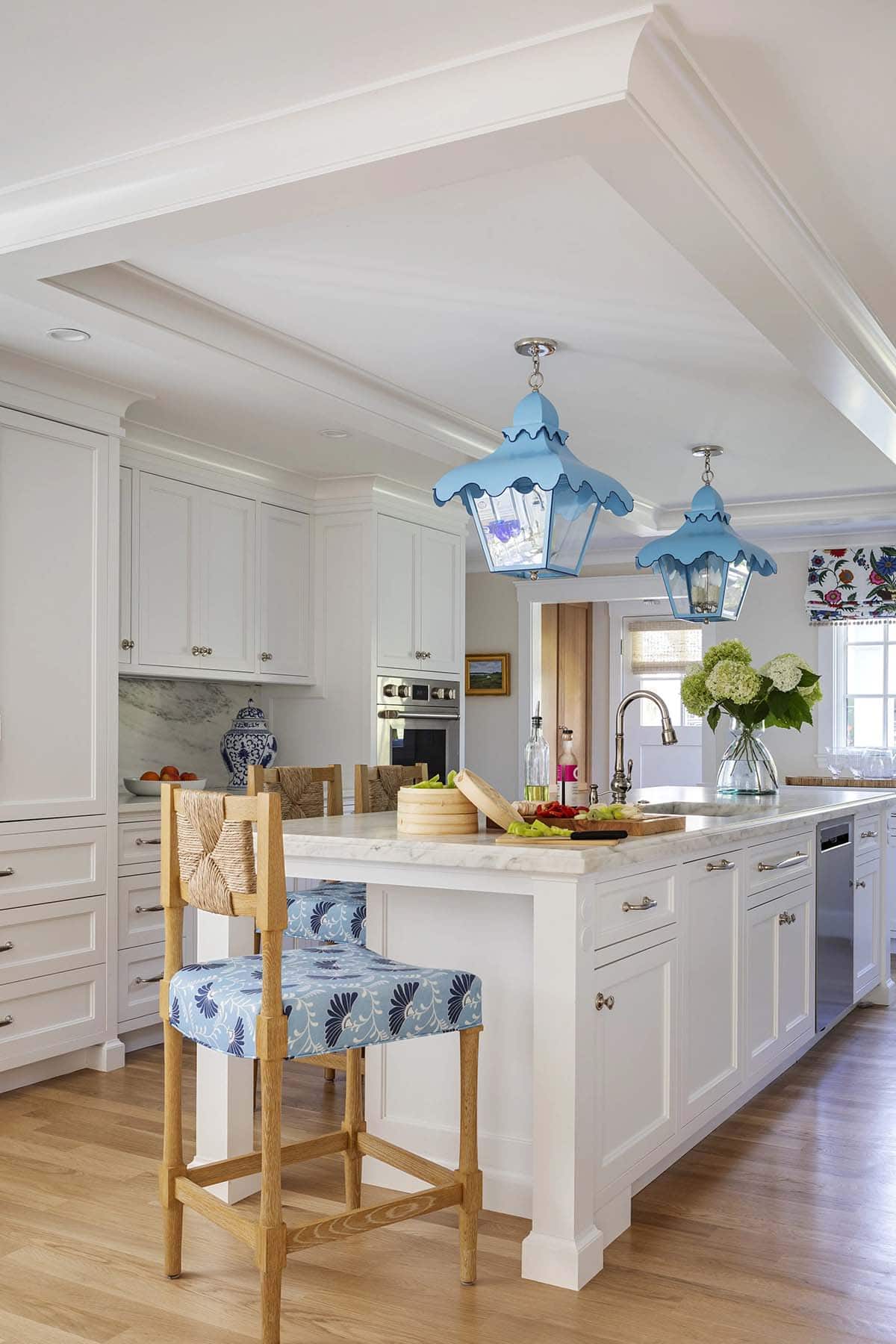 White kitchen island with woven counter stools in blue floral fabric under scalloped blue lanterns