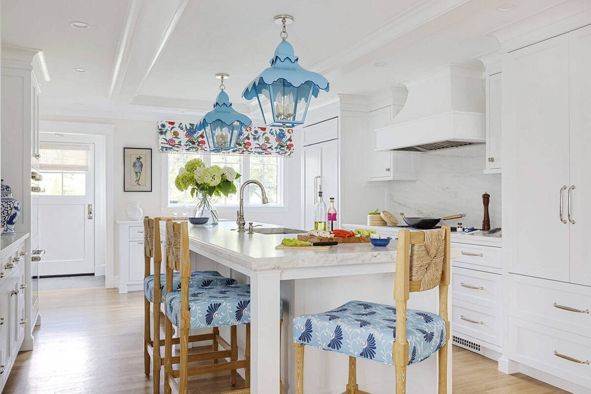 White kitchen with marble island, blue floral bar stools, and range hood in background