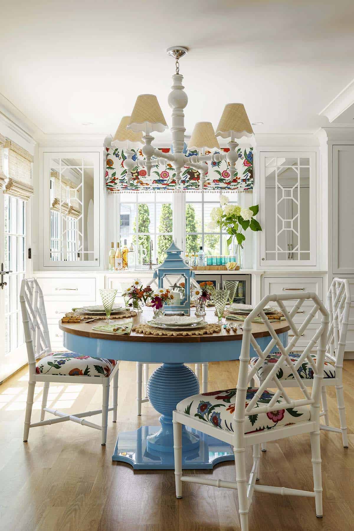 Round blue breakfast table with bamboo-style chairs in floral fabric under a white chandelier
