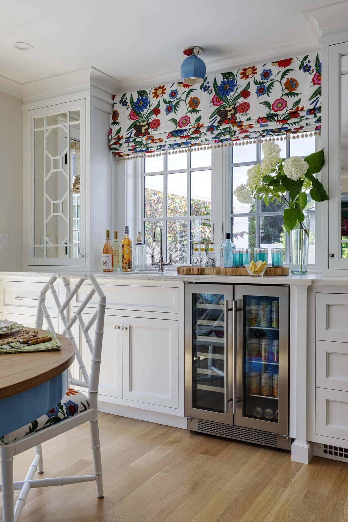 White butler's pantry with beverage fridge, bar cart, and bold floral roman shade