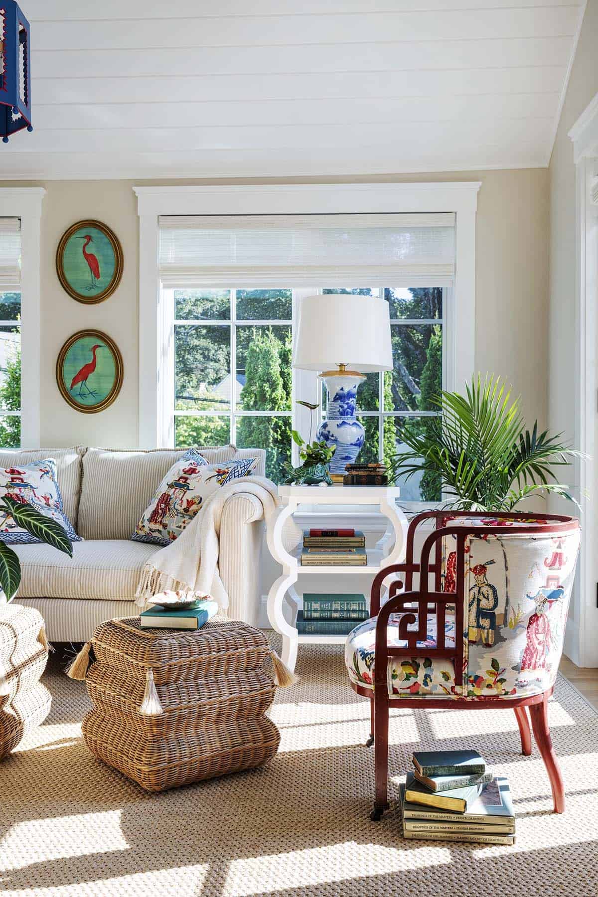 Sunroom seating area with striped sofa, wicker ottoman, and red chinoiserie-print armchair