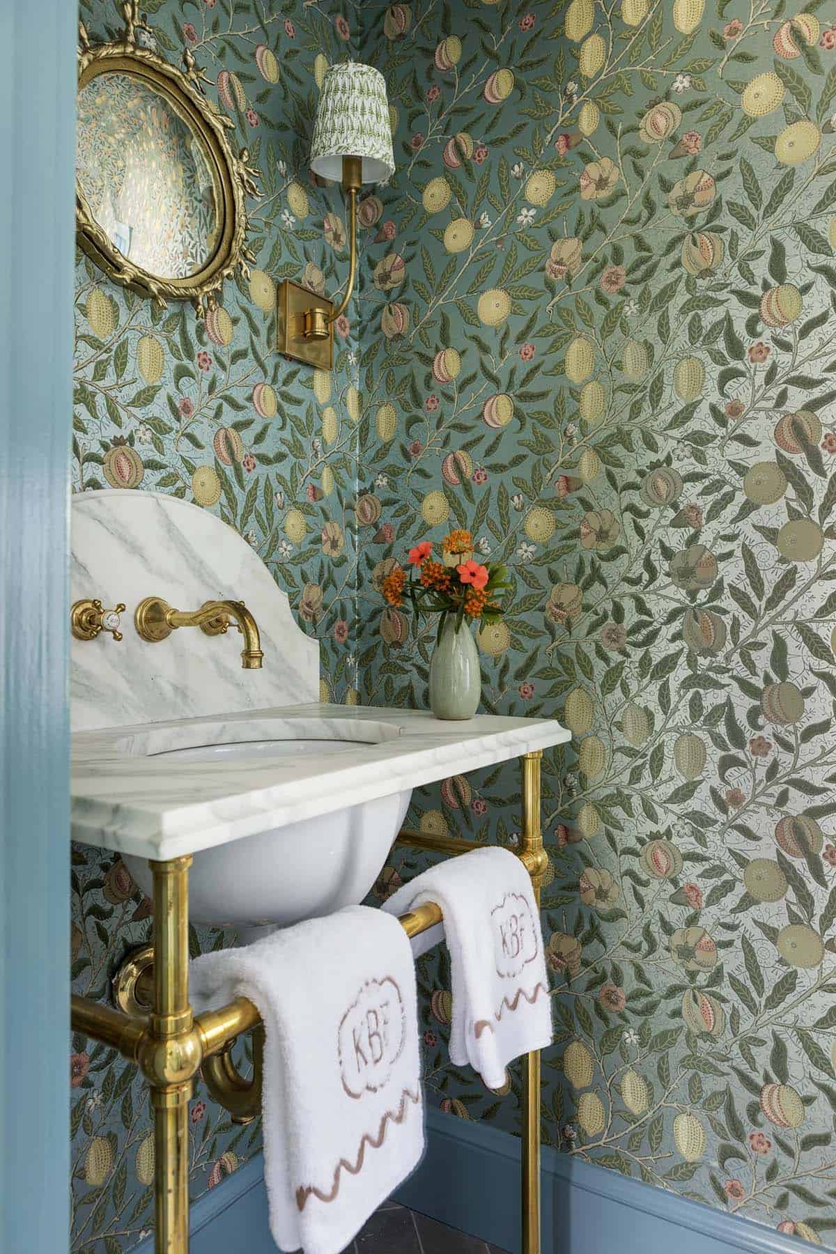 Powder room with botanical wallpaper, marble sink, brass fixtures, and monogrammed towels