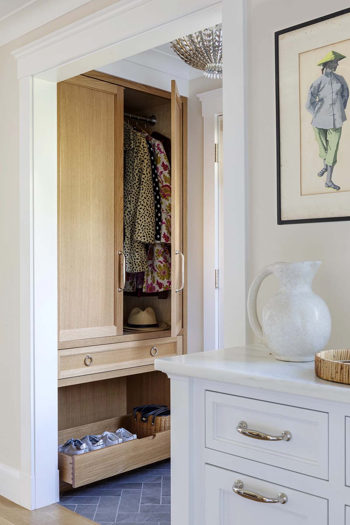Open mudroom closet with patterned coats, woven baskets, and built-in shoe drawer