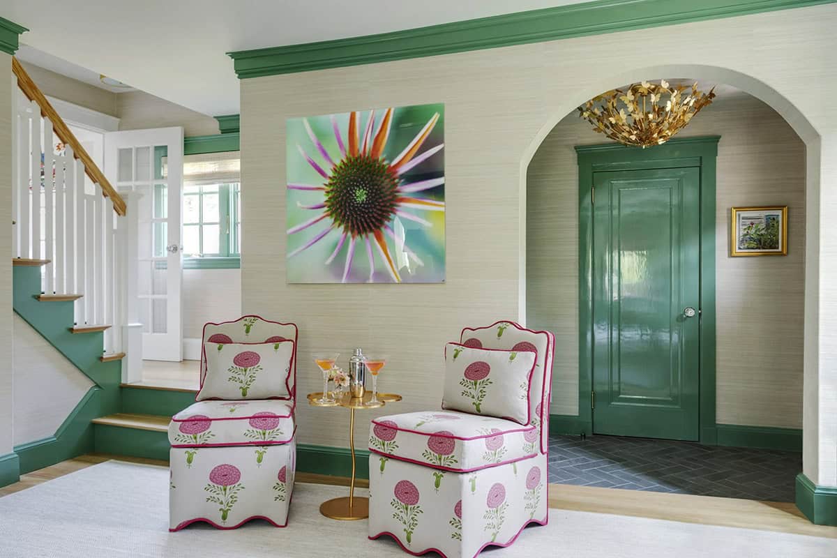 Green-trimmed entryway with pink floral slipper chairs and a glossy green door