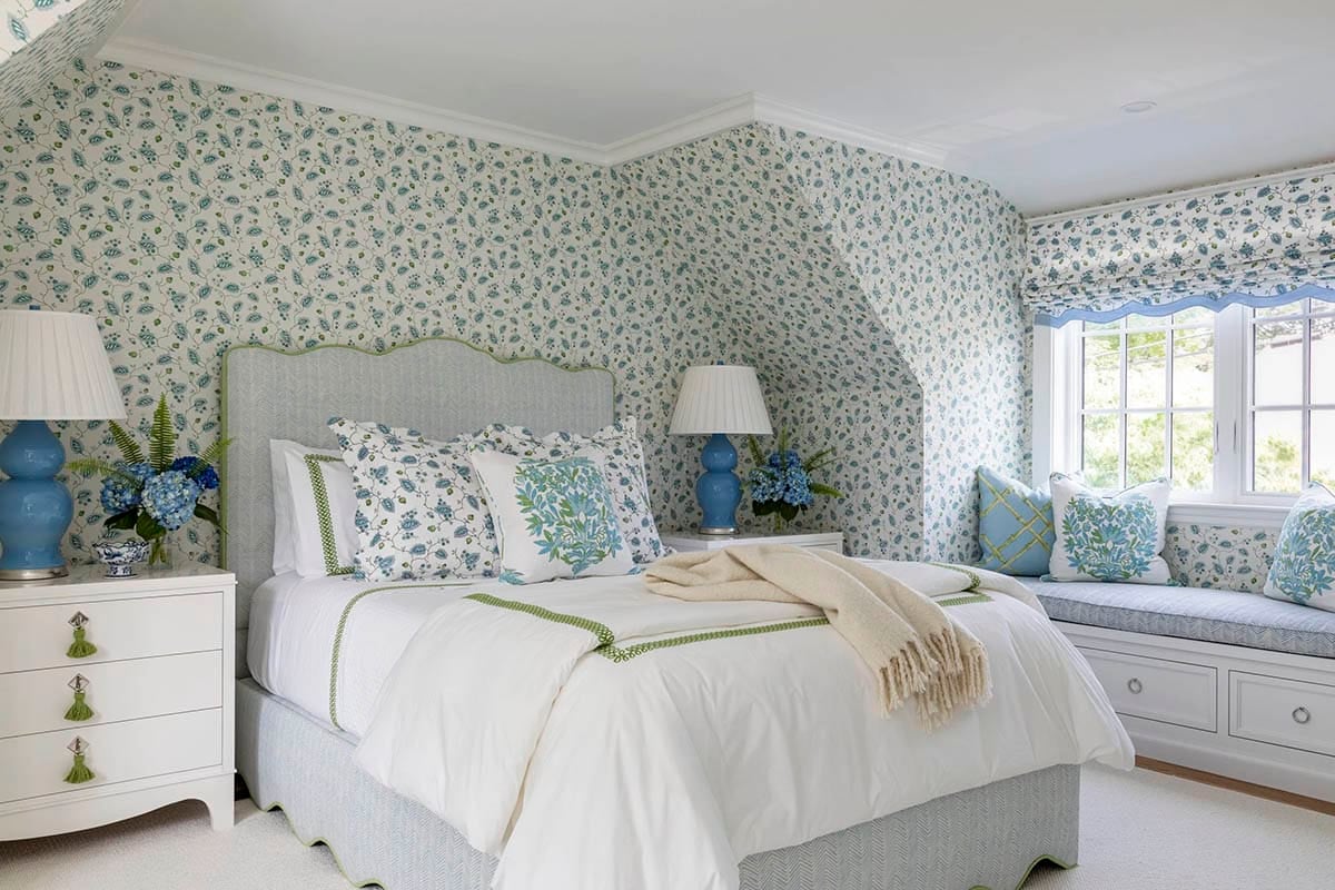 Bedroom with blue floral wallpaper, upholstered headboard, and matching window seat