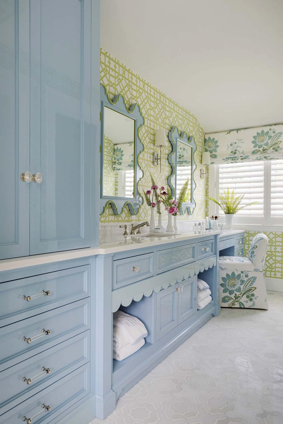 Blue primary bathroom with double vanity, scalloped mirrors, and green trellis wallpaper