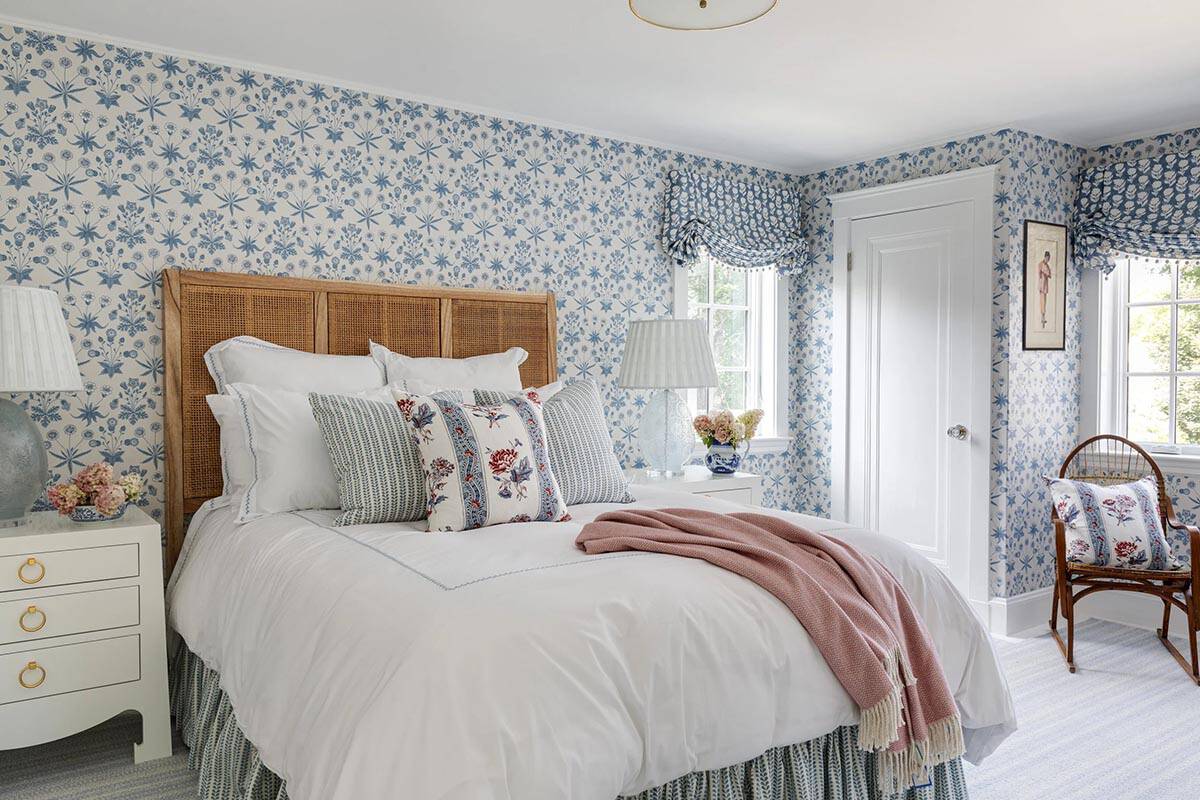 Bedroom with cane headboard, blue star-print wallpaper, and pink throw blanket on white bedding