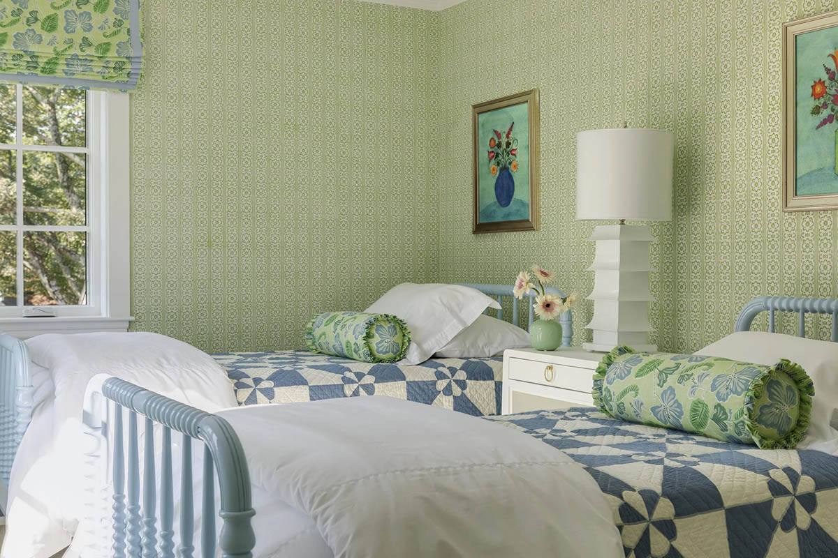 Twin bedroom with vintage-style blue spindle beds, green wallpaper, and patchwork quilts