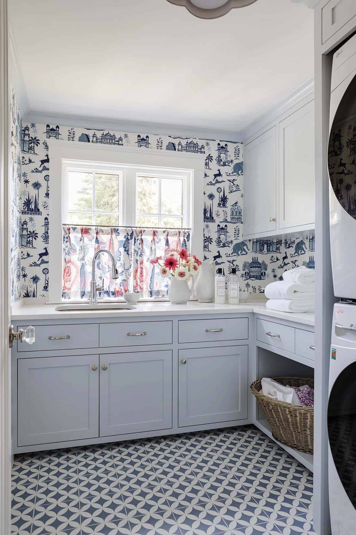 Laundry room with blue toile wallpaper, patterned tile floor, and stacked washer-dryer