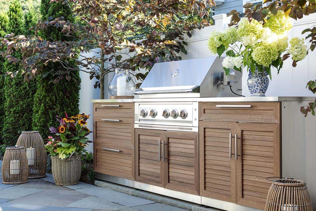 Outdoor kitchen with wood-look cabinetry, stainless grill, and potted hydrangeas