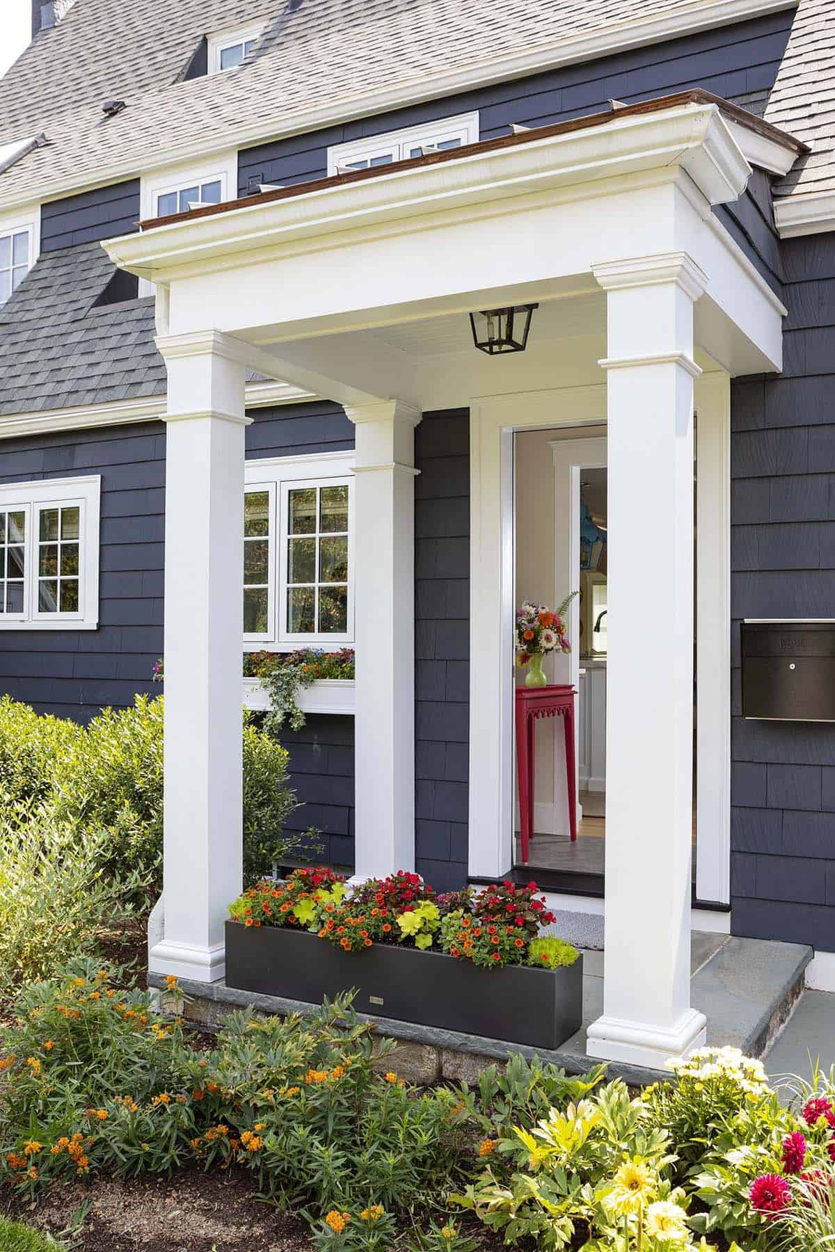 Front porch entrance with white columns, flower box, and glimpse of red console table inside