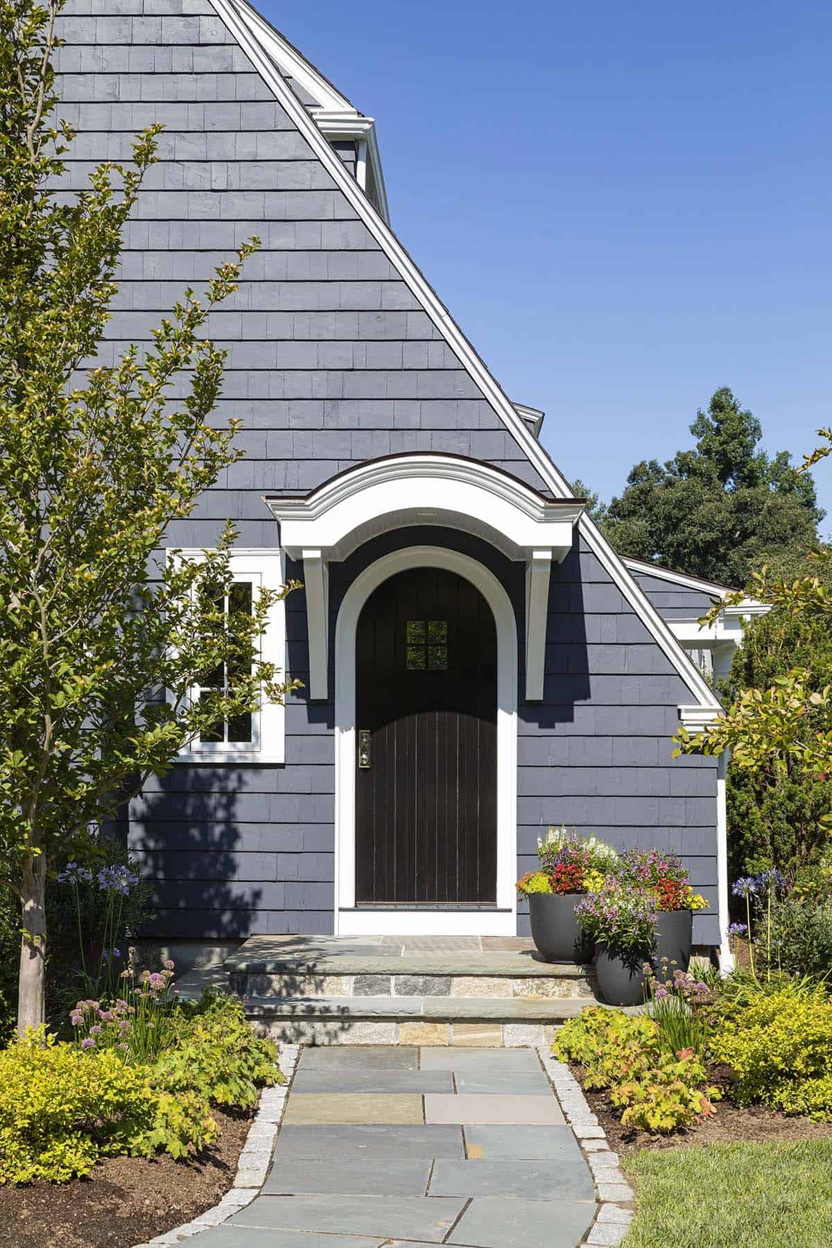 Gray shingle-style home exterior with arched dark front door and white trim detailing