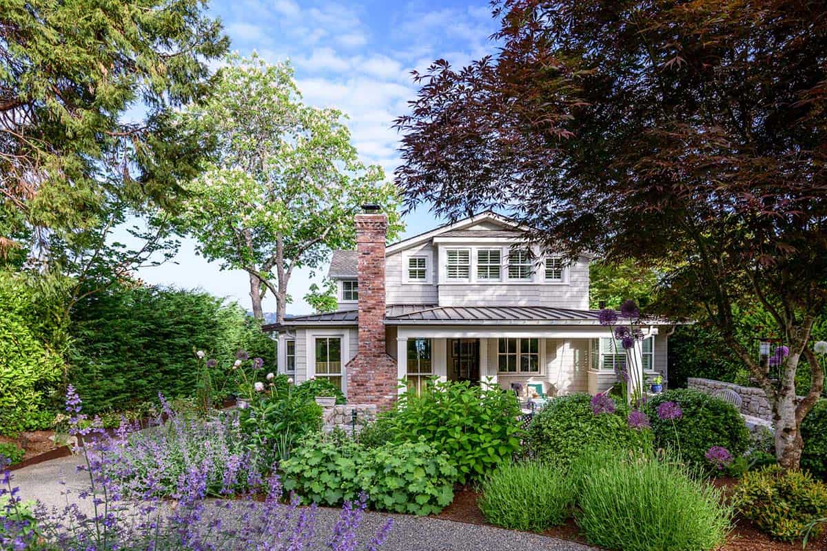 English cottage-style home exterior with brick chimney, shingle siding, and lush lavender garden