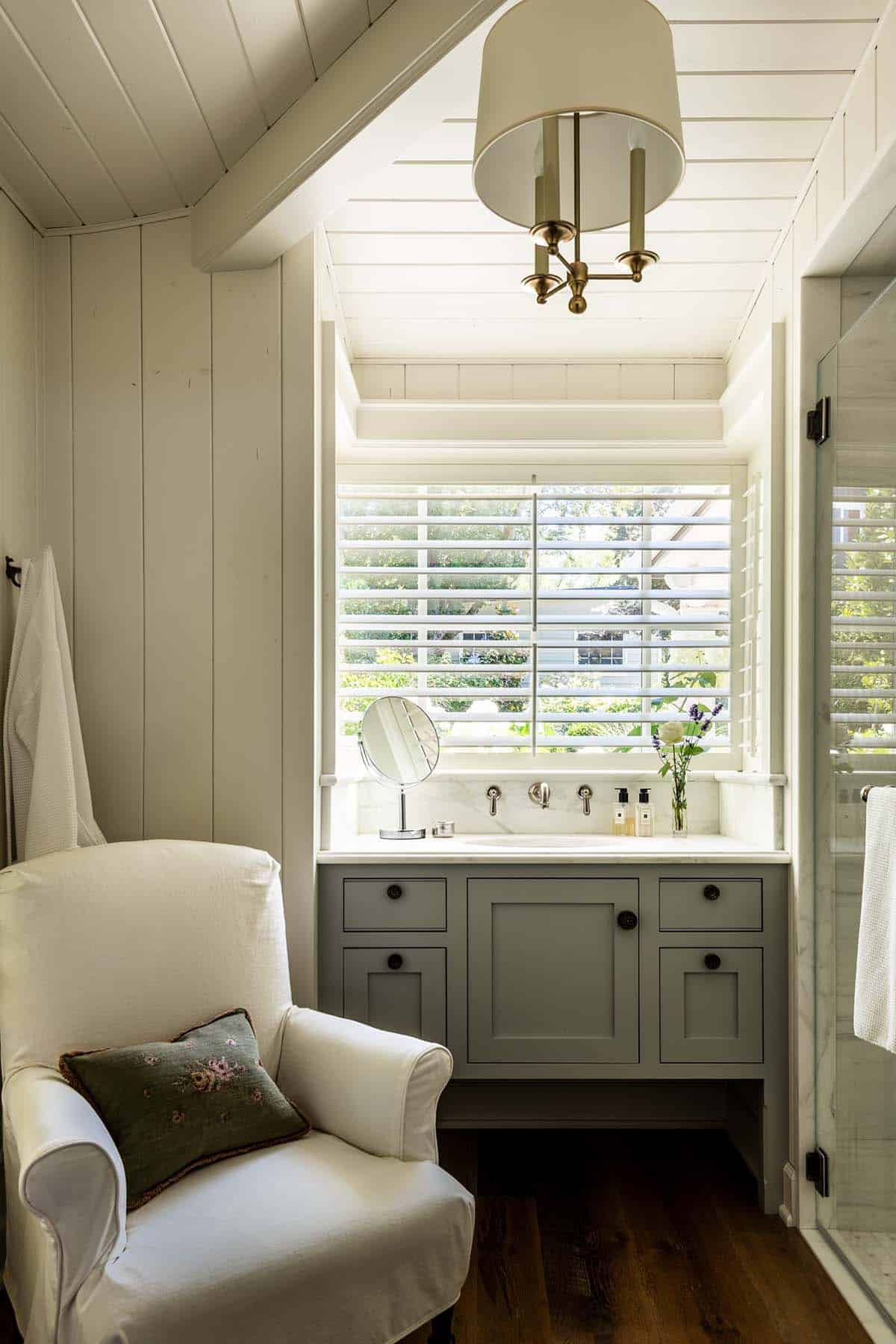 Bathroom nook with marble vanity, plantation shutters, and slipcovered chair