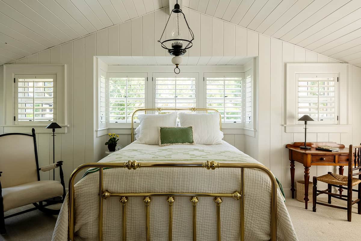 Bedroom with brass bed frame, vaulted shiplap ceiling, and antique lantern light