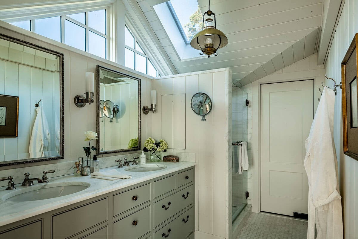 Double vanity bathroom with skylight, framed mirrors, and glass shower