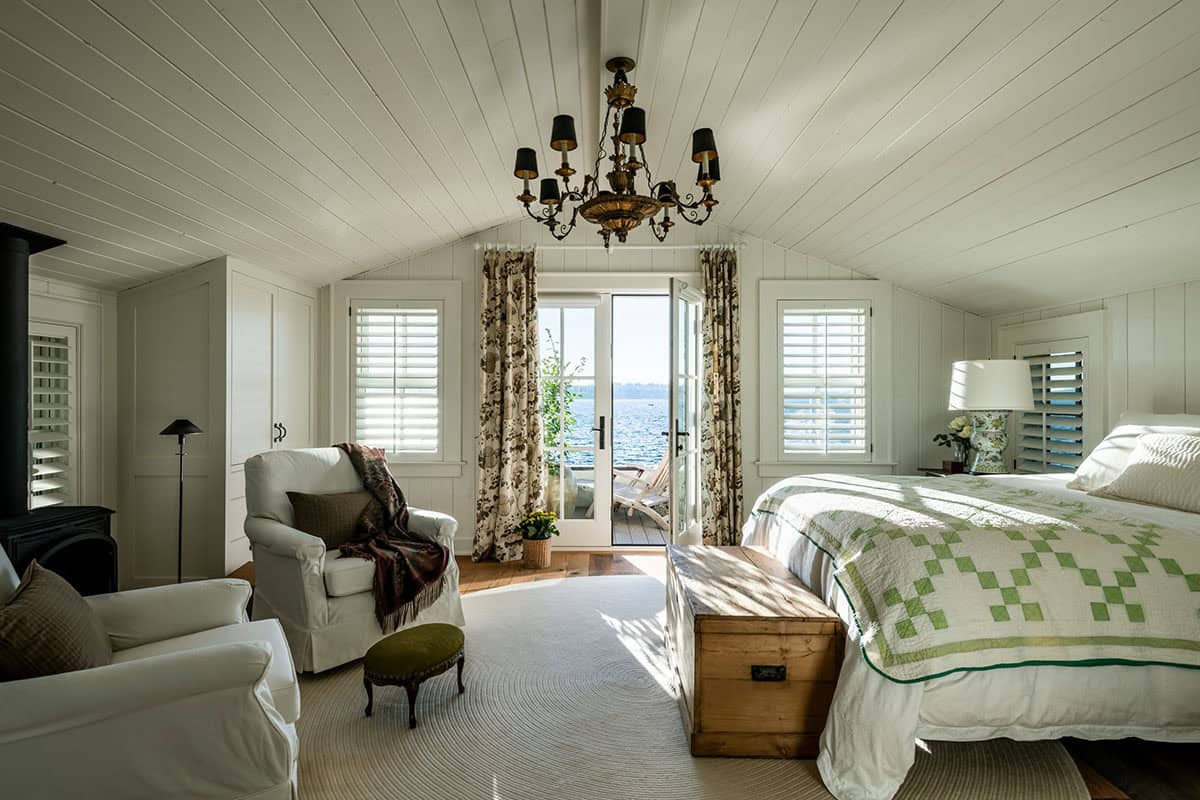 Vaulted bedroom with candle chandelier, seating area, and French doors to lake-view deck
