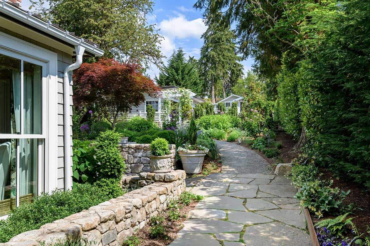 Flagstone garden path lined with stone walls, potted topiary, and lush landscaping