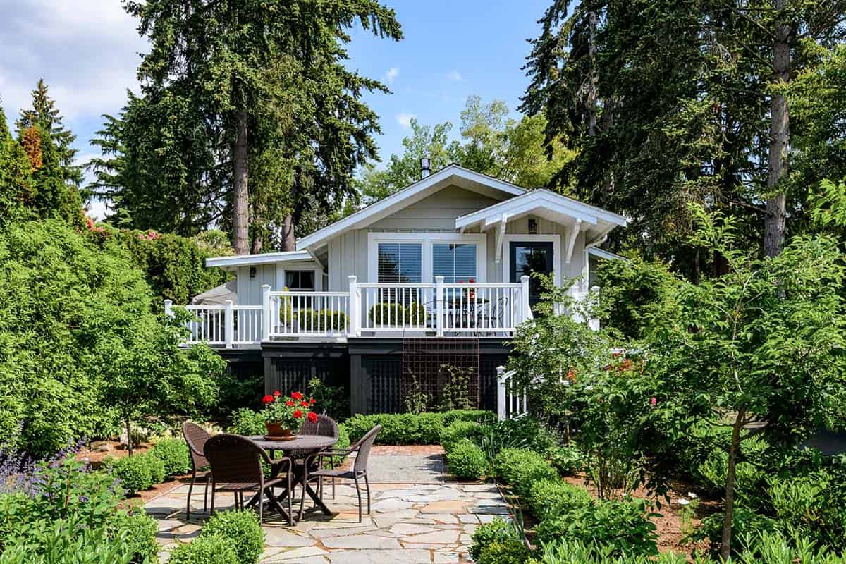 Guest cottage exterior with railed deck, patio seating, and surrounding evergreens