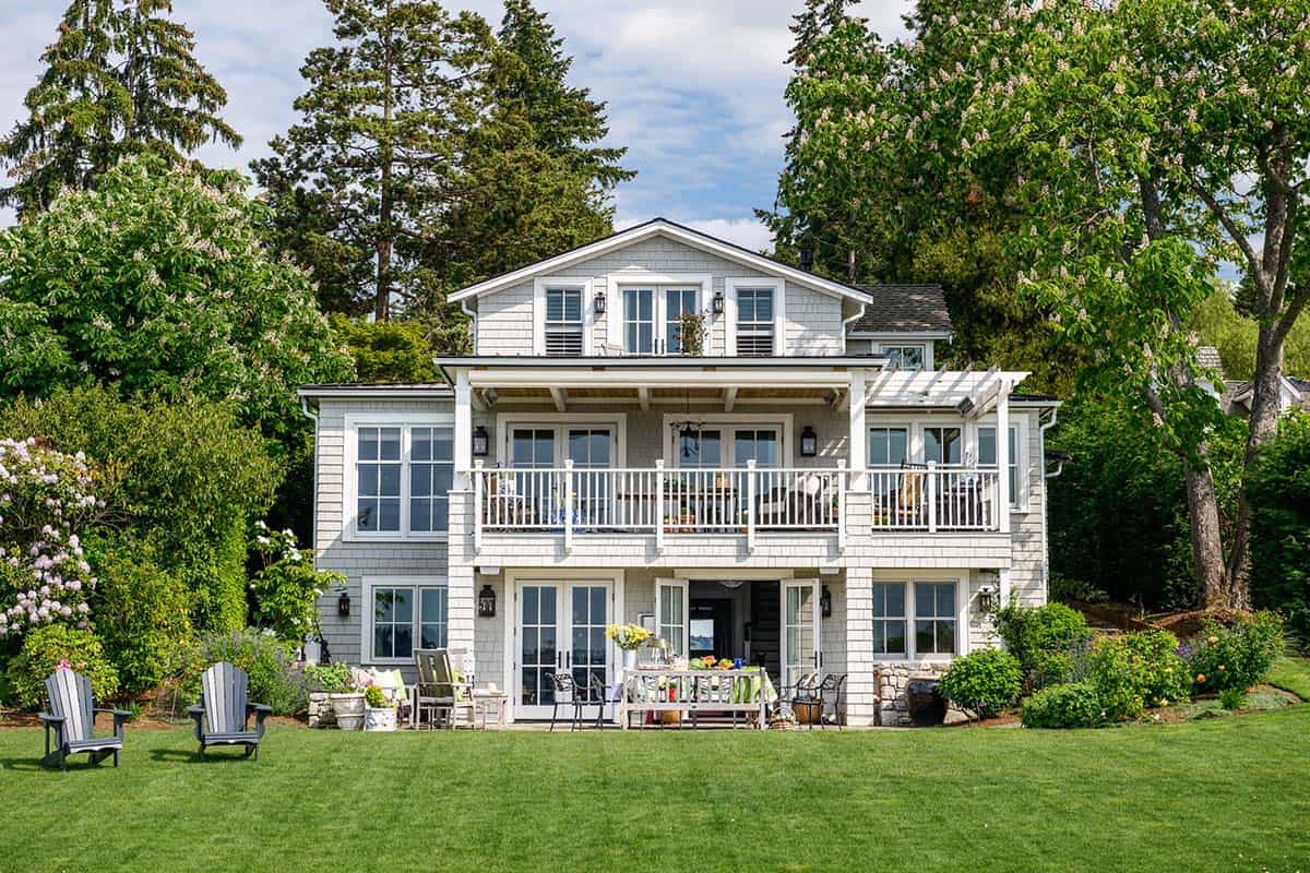 Rear view of shingle-style lakefront home with multiple balconies and manicured lawn